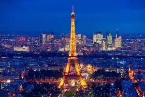 Eiffel Tower illuminated at night in Paris, France, with city skyline background.