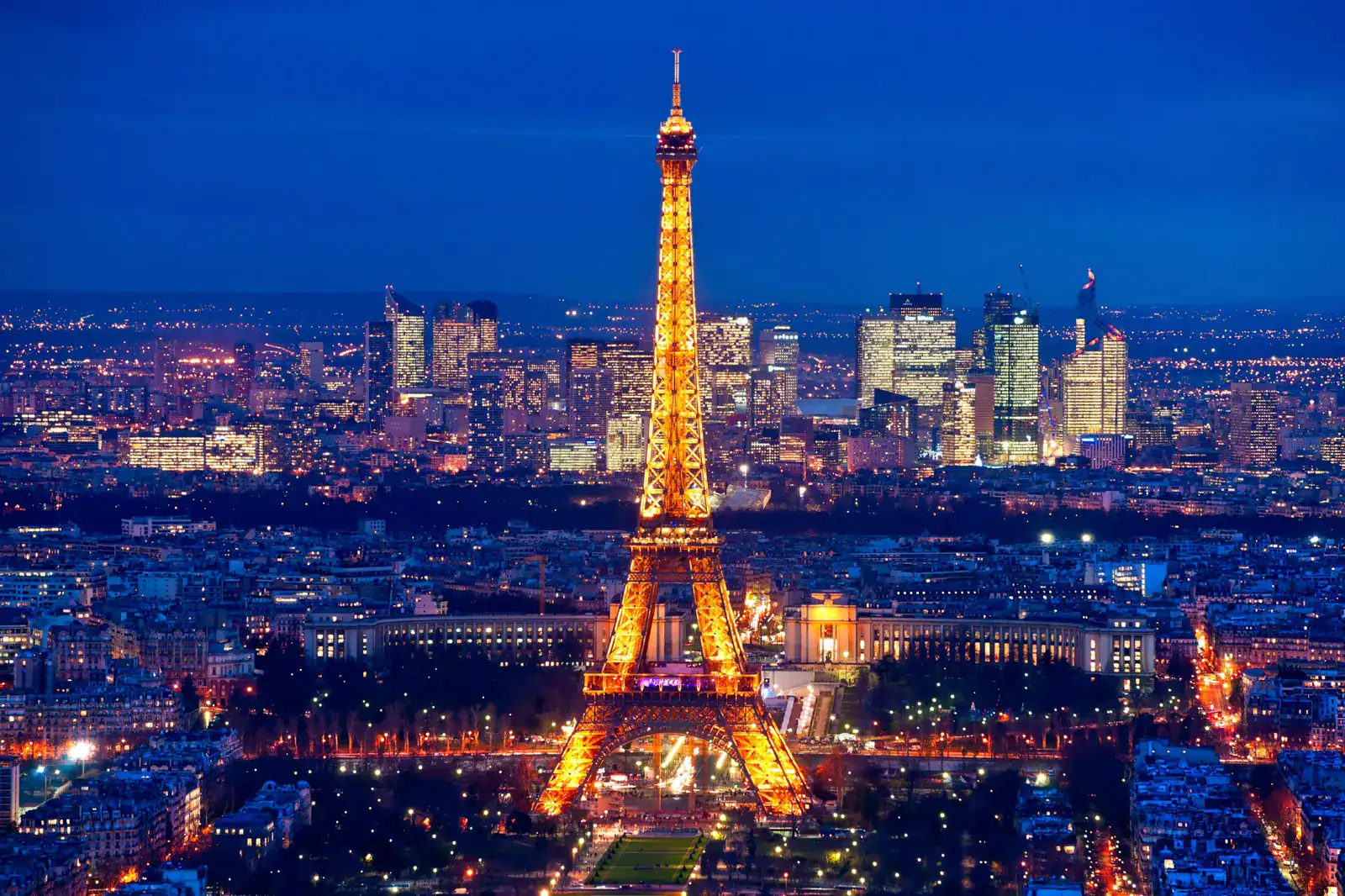 Eiffel Tower illuminated at night in Paris, France, with city skyline background.